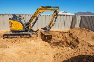 Picture of a piece of machinery digging up a yard to install a swimming pool. 